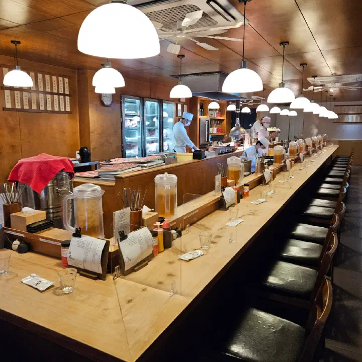 Long counter seating wrapped around the open kitchen inside Tonshou Gwangan, with chefs preparing tonkatsu