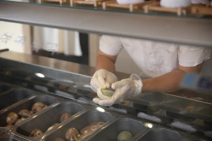 A gloved staff member at Horangi Jella Tteok wrapping a ball of gelato in a thin glutinous rice cake skin