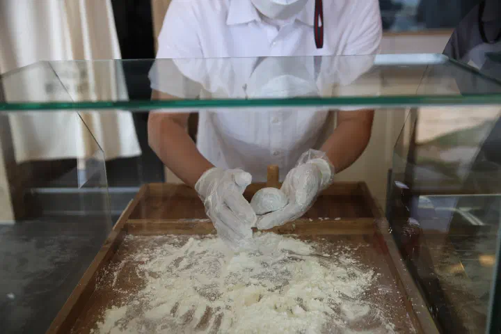 A staff member hand-shaping a jella tteok in a tray of glutinous rice flour at Horangi Jella Tteok