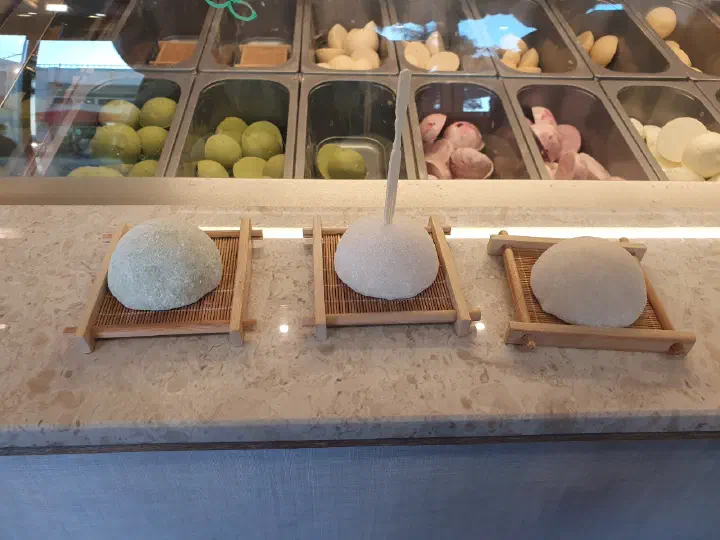Matcha, salted milk, and pistachio jella tteok lined up on bamboo trays at the Horangi Jella Tteok counter
