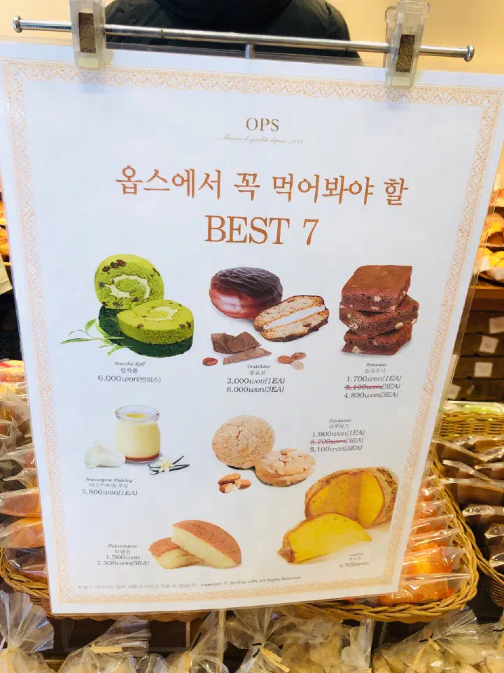 OPS Best 7 menu board in the bakery showing maccha roll, mascarpone pudding and hagwonjeon with prices