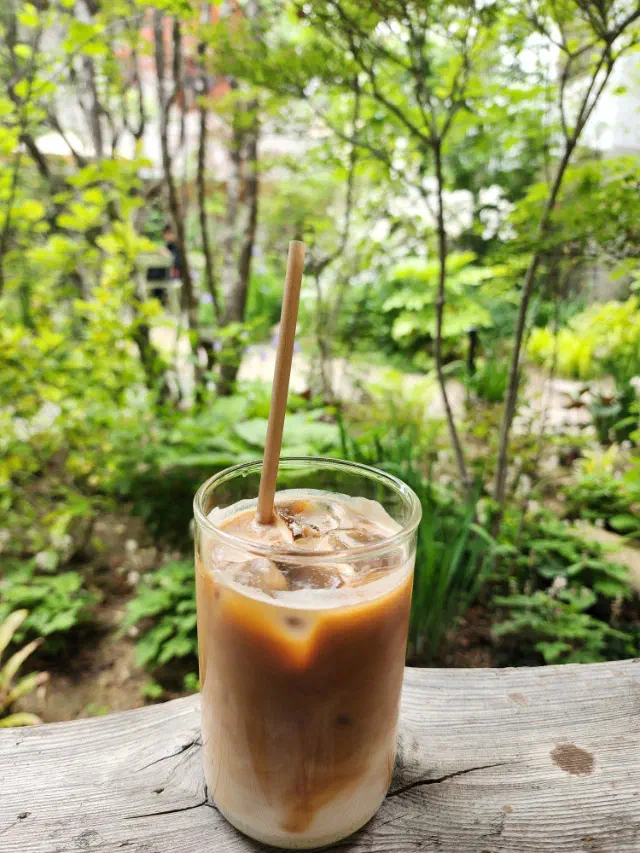 Iced latte from Momos Coffee on a wooden ledge with the green garden in the background
