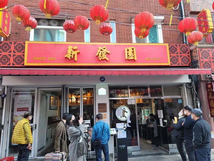 Red signboard and lanterns at the Sinbalwon dumpling house entrance in Busan Chinatown, with customers waiting outside