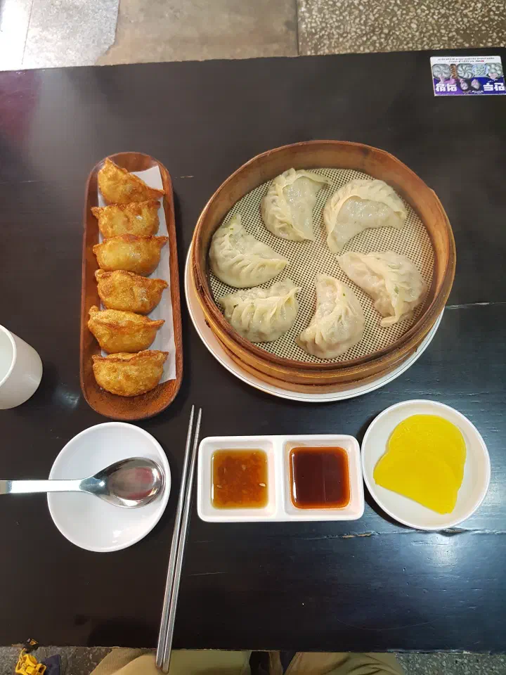 Full table at Sinbalwon with fried dumplings, steamed dumplings in a bamboo basket, dipping sauces and pickled radish