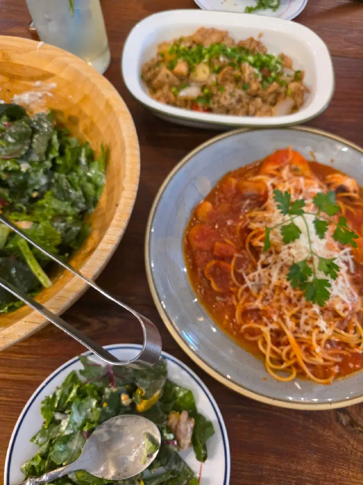 A spread of salad, pasta and fried rice on a wood table at Cheongchun Kitchen