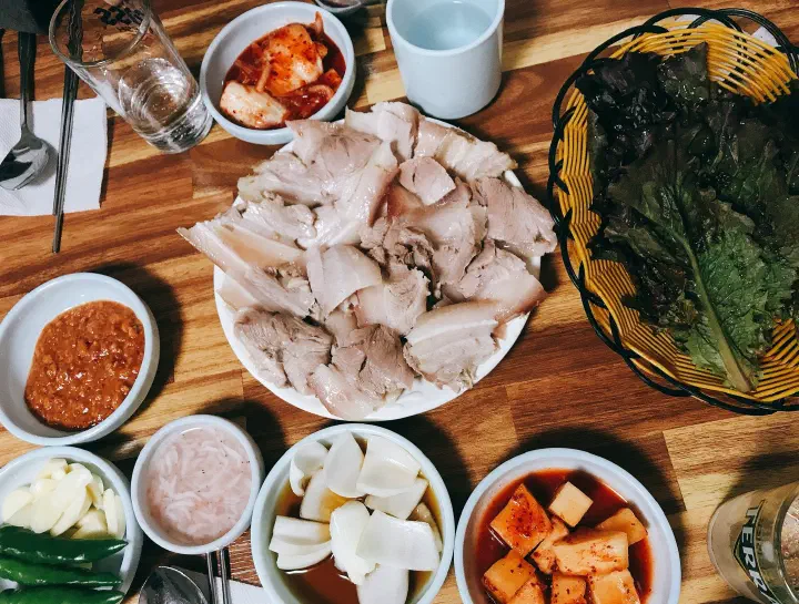 A plate of boiled pork suyuk with lettuce, kimchi and side dishes