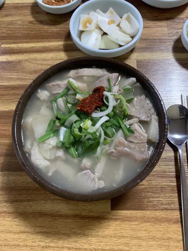 A clear-broth pork gukbap in a stone bowl with pickled onion
