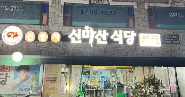 Neon sign and entrance of Shinsongja Sinmasan Sikdang with its ginseng-pig logo