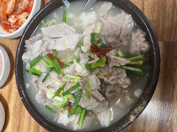 An earthenware bowl of pork gukbap loaded with meat