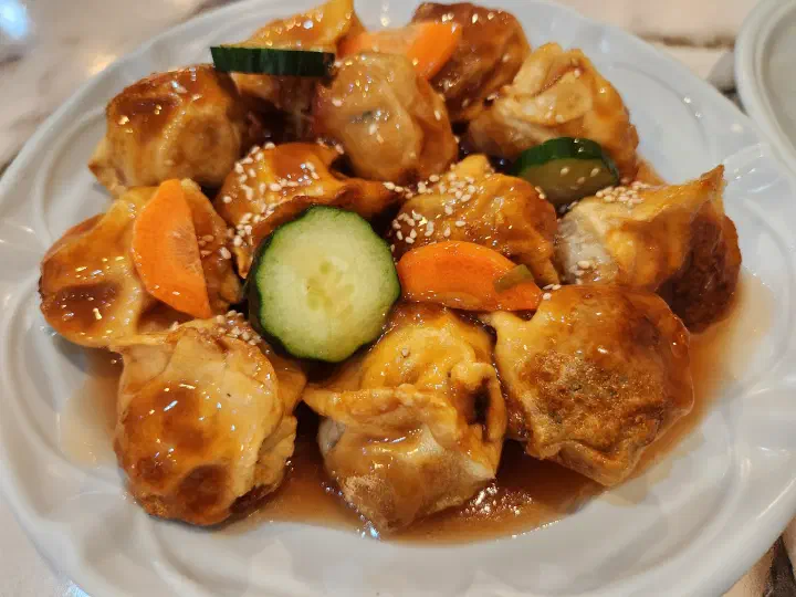Taesan Mandu close-up of tangsu-mandu, sauce-coated dumplings topped with sesame seeds, cucumber, and carrot