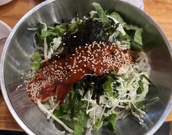 Bowl of Kimhwa Kalguksu bibimguksu with red sauce and toasted sesame seeds
