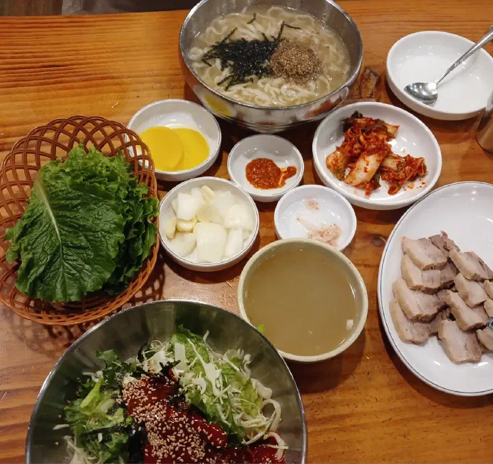 Full table setting at Kimhwa Kalguksu with noodle soup, cold noodles, boiled pork, lettuce and kimchi