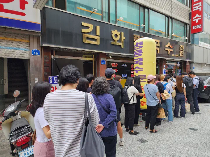 Customers waiting in a long line outside Kimhwa Kalguksu at lunchtime