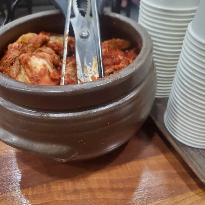 Crock of fiery house kimchi self-serve on a table at OC Kalguksu