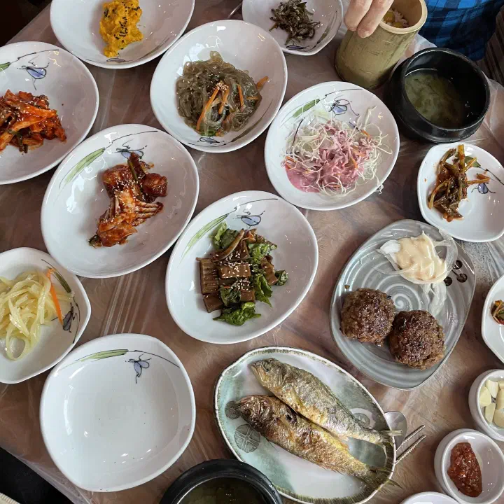 Spread of Korean side dishes including bamboo shoots, japchae and grilled fish