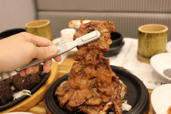 Charcoal pork ribs lifted with tongs at Hansangeun Daetongbapjip