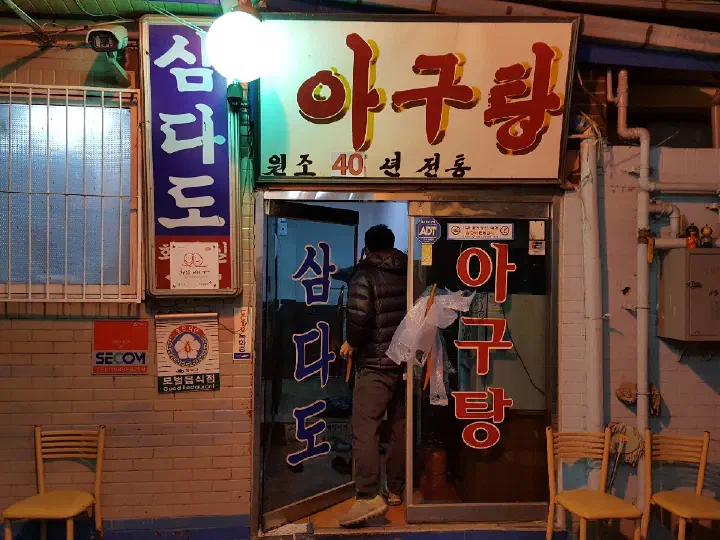 Exterior and illuminated agutang sign of Samdado monkfish restaurant in a Gangbuk-gu alley, Seoul