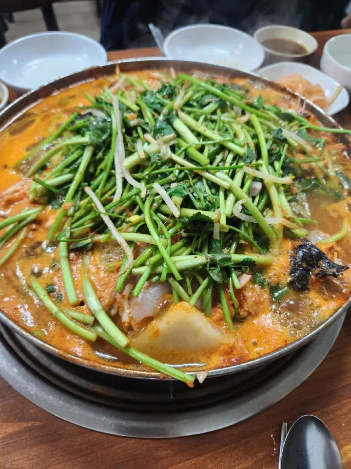Red spicy monkfish stew with added offal bubbling under a layer of minari
