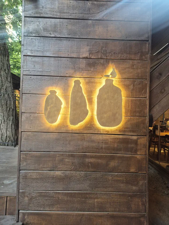 Backlit oil bottle silhouettes mounted on the dark timber exterior wall of Apgujeong Sanghoe in Seoul