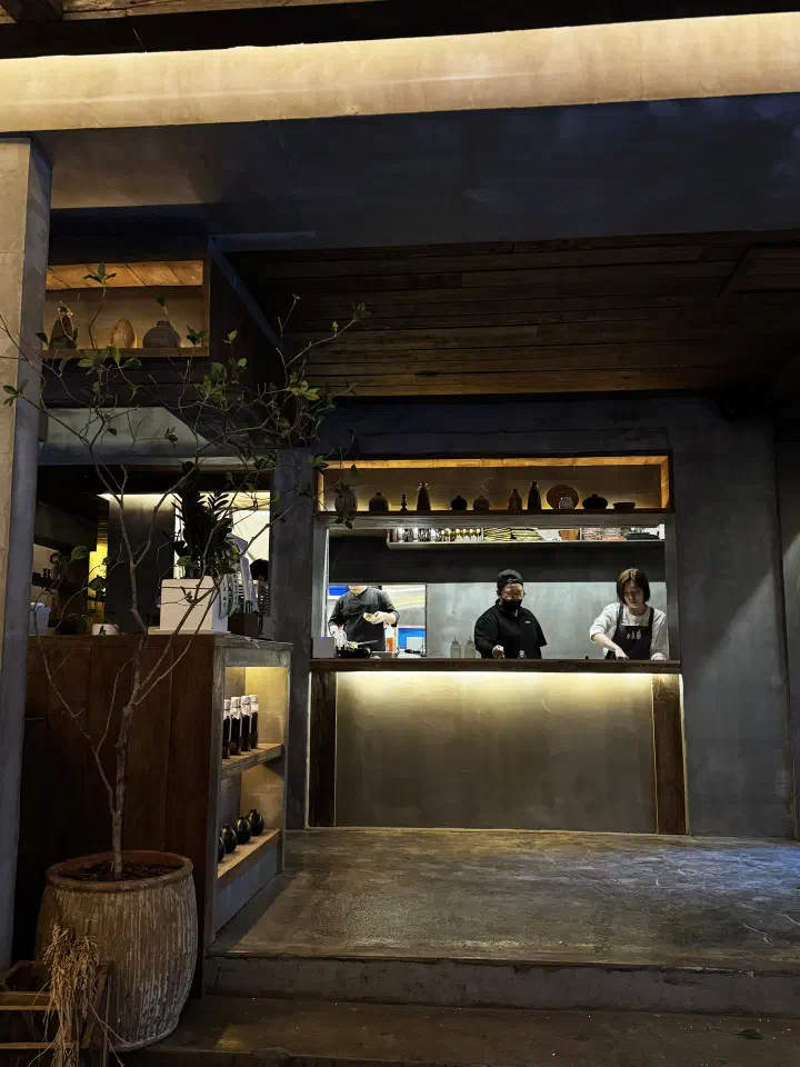 Staff working behind the open kitchen counter at Apgujeong Sanghoe, next to a shelf of bottled house-pressed oil