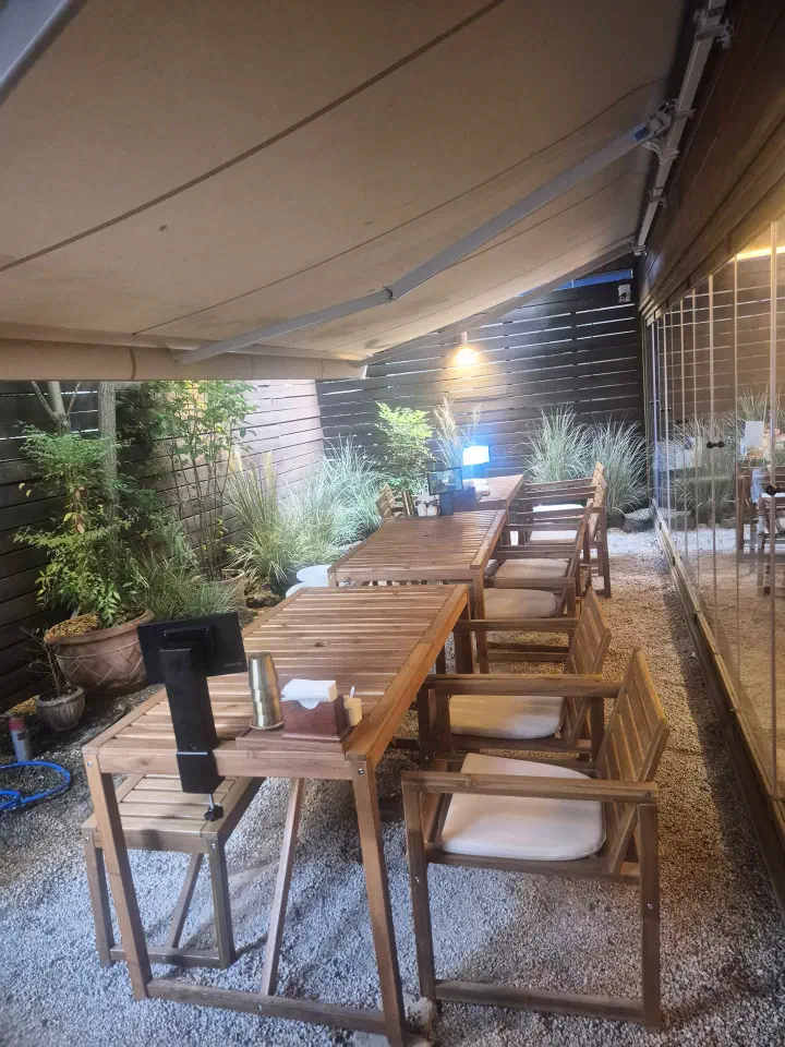 Outdoor terrace seating at Apgujeong Sanghoe under a retractable awning, framed by planted grasses