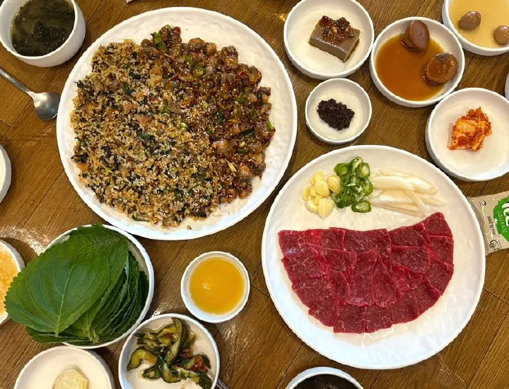 Overhead view of Dokdone’s two-person set with cockle rice bowl, raw beef and ten side dishes