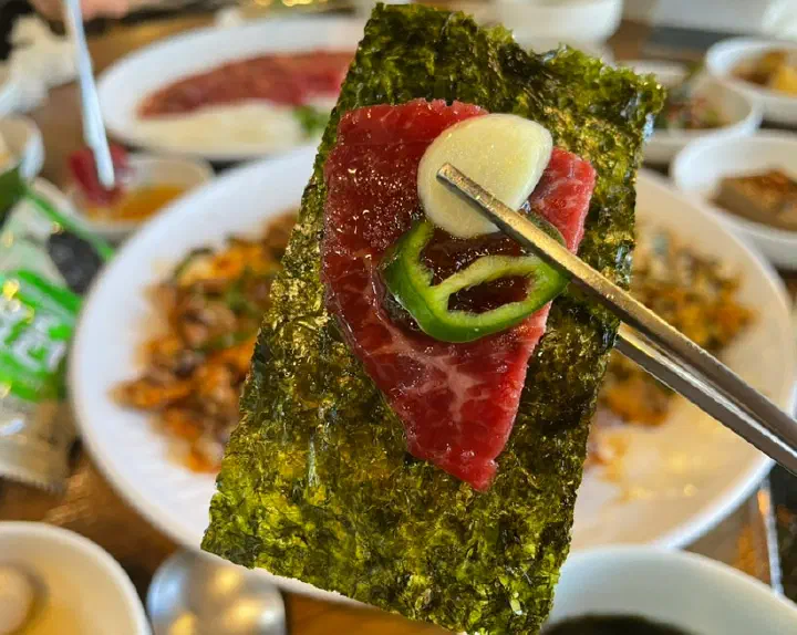 Raw beef topped with garlic and green chili on a sheet of seaweed, held with chopsticks