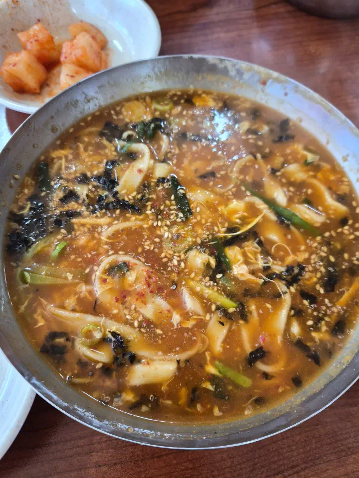 Single bowl of jang kalguksu with a side dish of kkakdugi radish kimchi
