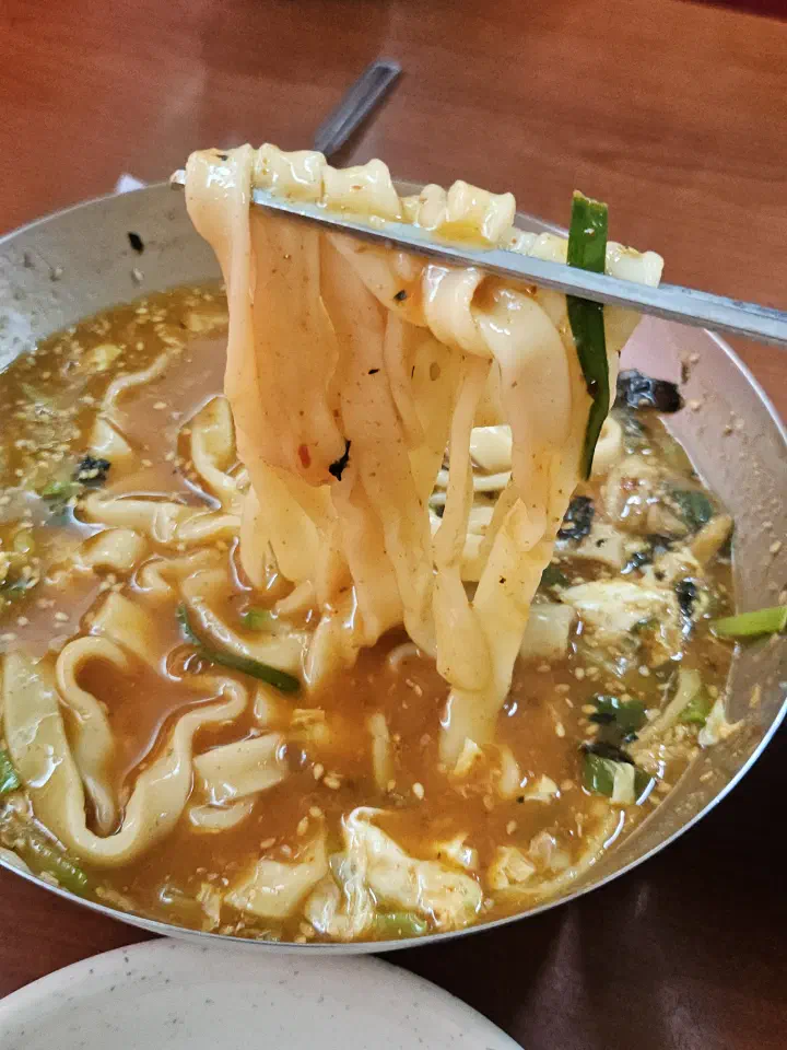 Wide, thick knife-cut kalguksu noodles lifted from the broth with chopsticks