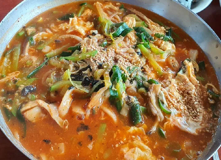 Close-up of jang kalguksu broth with sliced zucchini and swirled egg