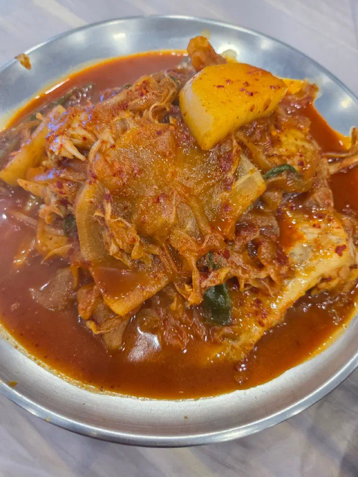 Overhead view of braised skate with chunks of potato submerged in red broth