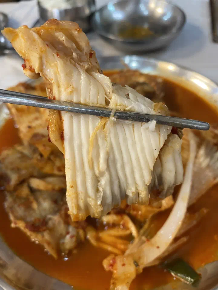 Chopsticks lifting a piece of braised skate that separates into long crab-like strands