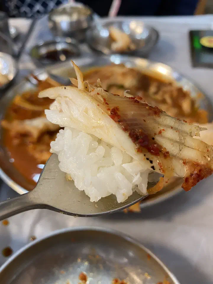 A spoonful of white rice topped with a chunk of braised skate