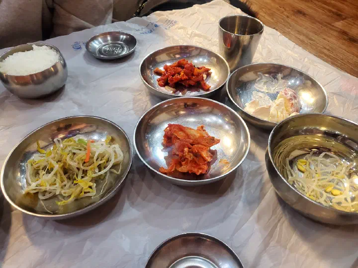 Side dishes and a bowl of rice on a table covered with disposable plastic sheeting