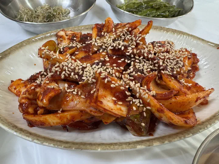 Close-up of thick squid pieces in chili sauce topped with toasted sesame seeds