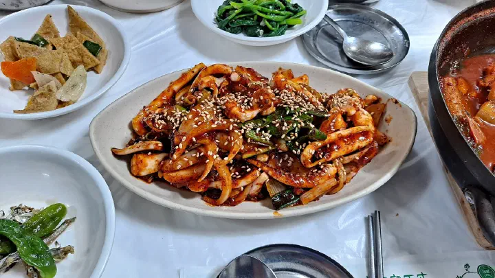Platter of stir-fried squid surrounded by banchan and the hairtail pot on the same table
