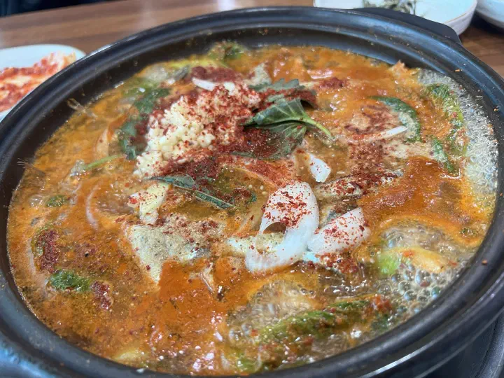Geoje anchovy stew as freshly served, topped with chili powder, minced garlic, and perilla leaves in a generous broth