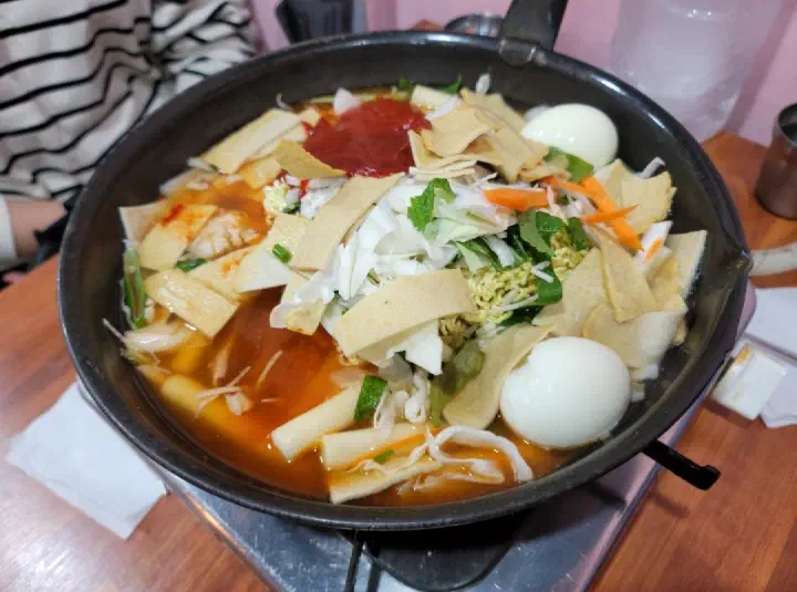 A pot of jeukseok tteokbokki loaded with ramyeon sari and eggs before the burner is lit
