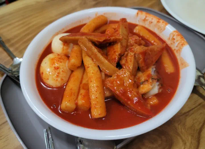 A bowl of modern plate-style tteokbokki coated in thick, deep red sauce