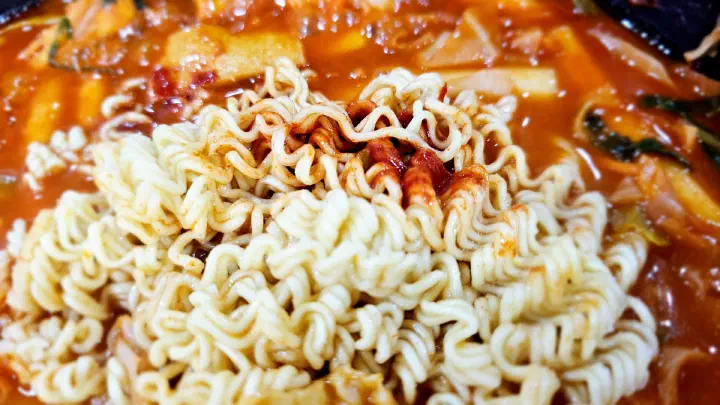 Close-up of ramyeon noodles cooking in the red tteokbokki sauce