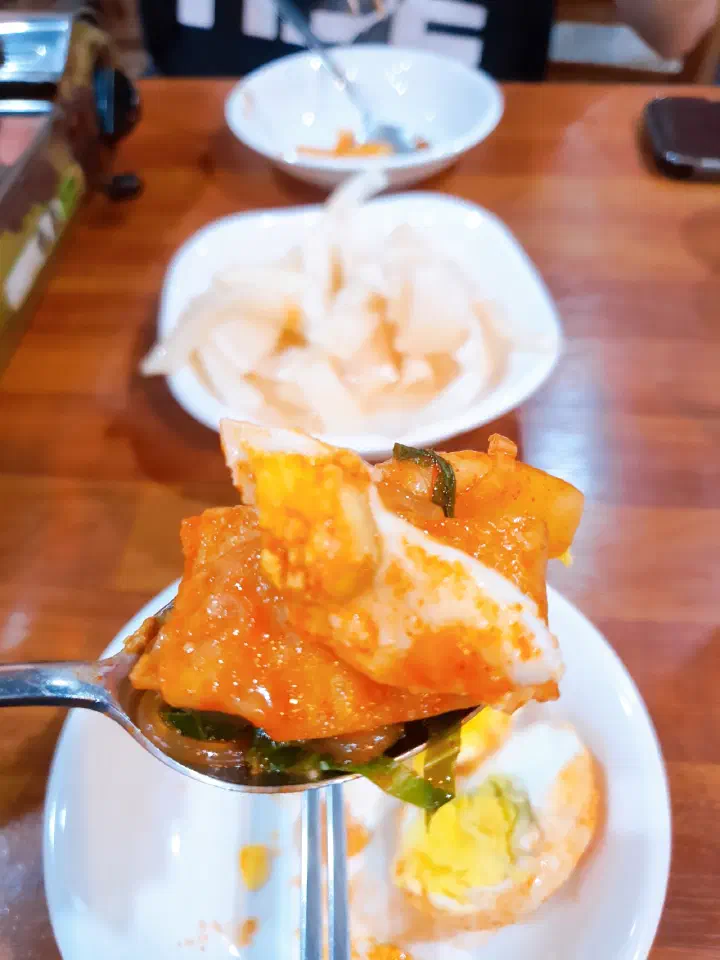 A spoonful of tteokbokki with the shop&rsquo;s homemade mu-kimchi radish in the background