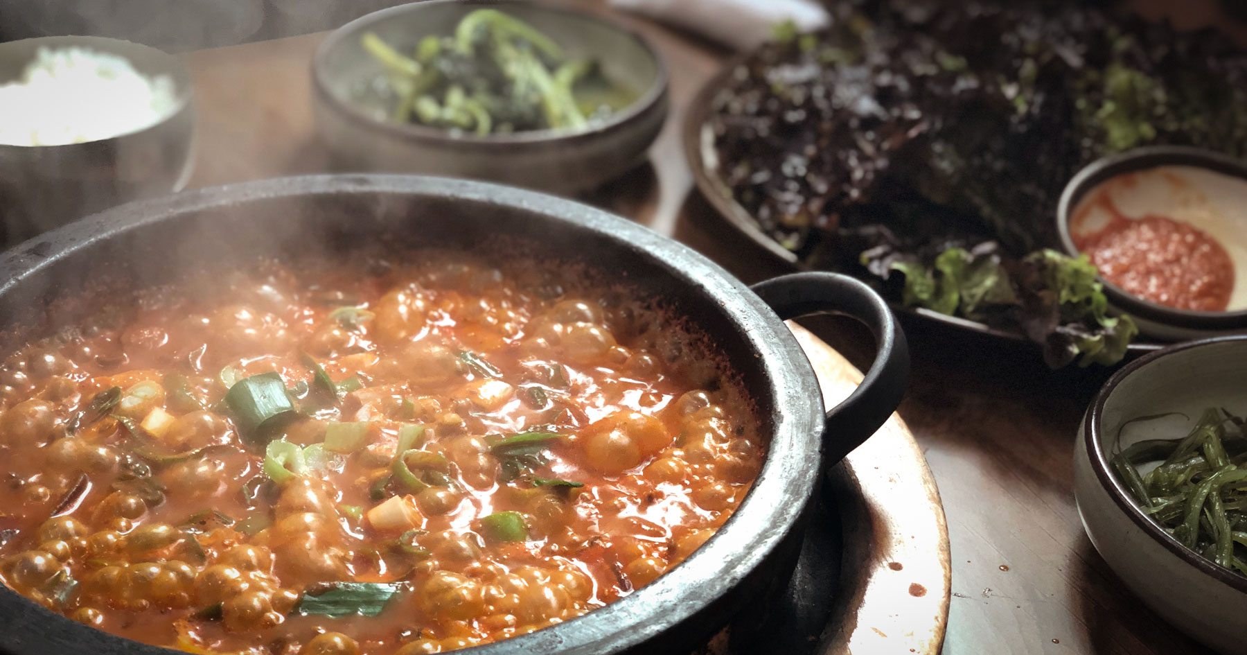 Sizzling anchovy ssambap on a hot stone plate with fresh lettuce at Bomnae Jangyu