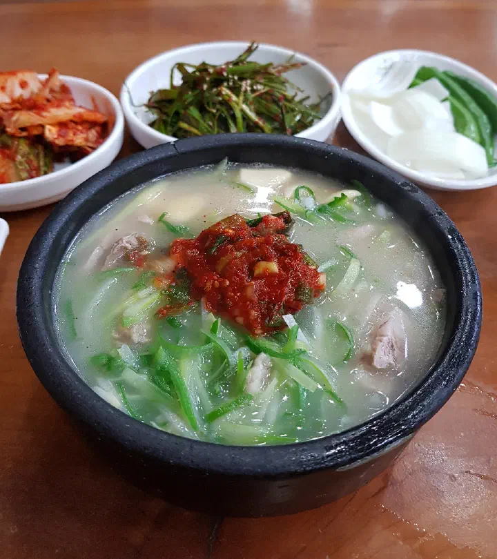 Close-up of clear dwaeji gukbap pork rice soup topped with shredded scallion and red dadaegi at Miryang Dwaeji Gukbap in Gimhae