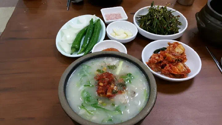 Dwaeji gukbap served with side dishes of buchu muchim seasoned garlic chives, kimchi, and onion at Miryang Dwaeji Gukbap