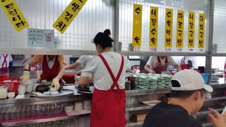 Staff ladling bowls of soup at the busy kitchen counter of Miryang Dwaeji Gukbap