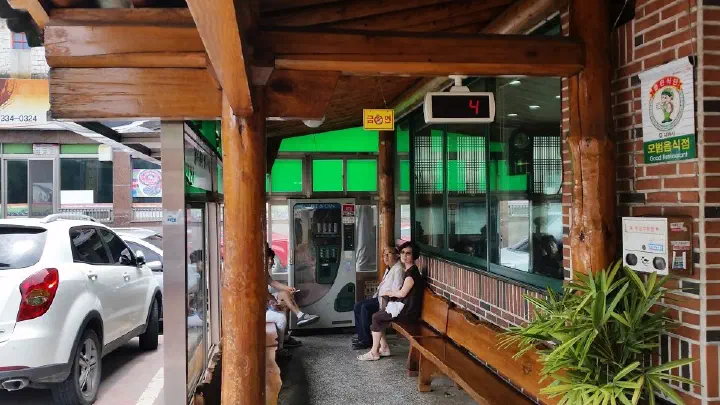 Covered outdoor waiting area with a number-display board and bench at Miryang Dwaeji Gukbap