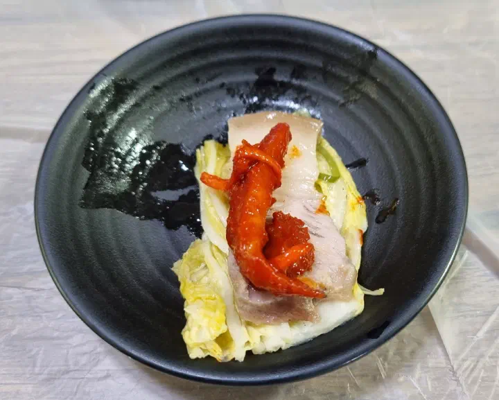 A bite of Baekchon Makguksu pyeonyuk and seasoned pollack wrapped in white kimchi