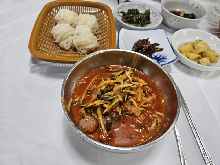 Mulhoe served with a basket of somyeon noodles and Korean side dishes at Gwangbeomine Hoetjip
