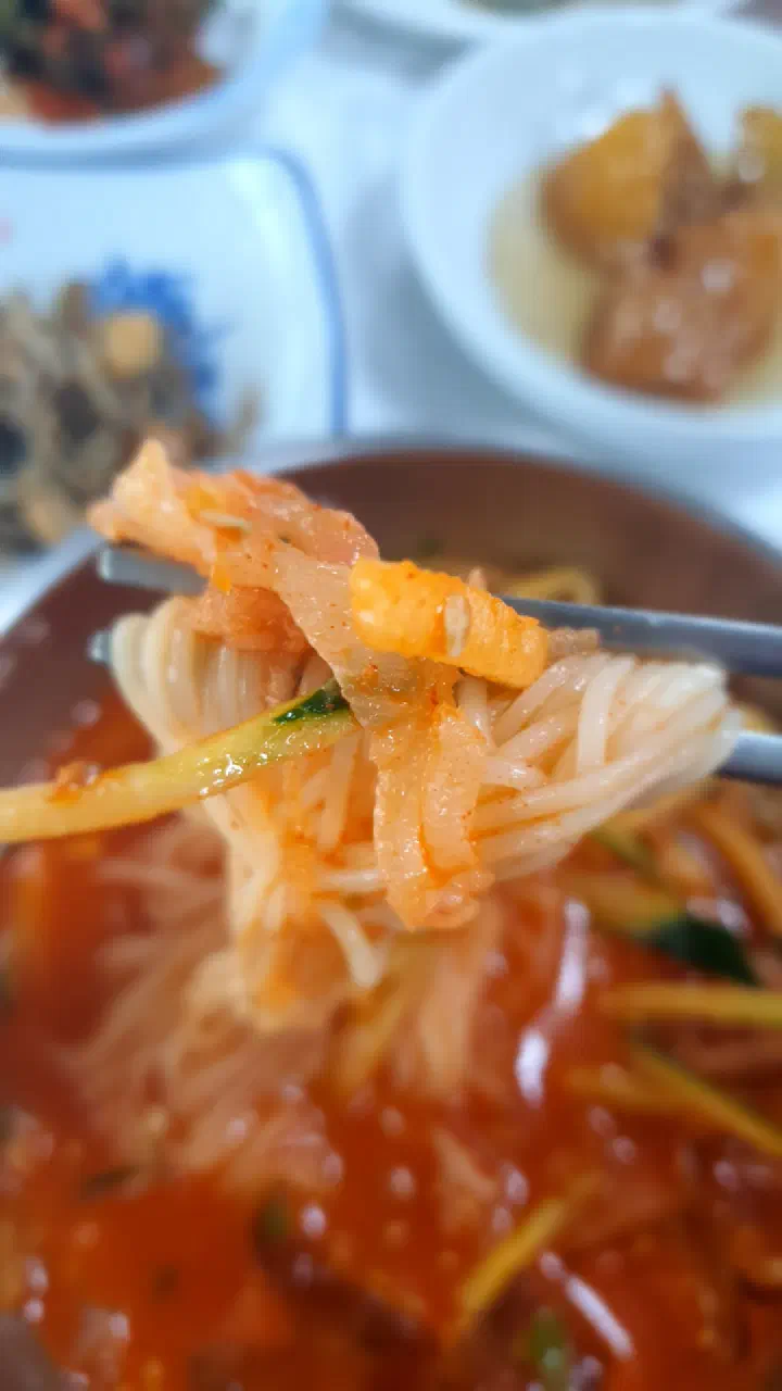 Chopsticks lifting flatfish sekkosi and somyeon noodles from a bowl of Gwangbeomine mulhoe