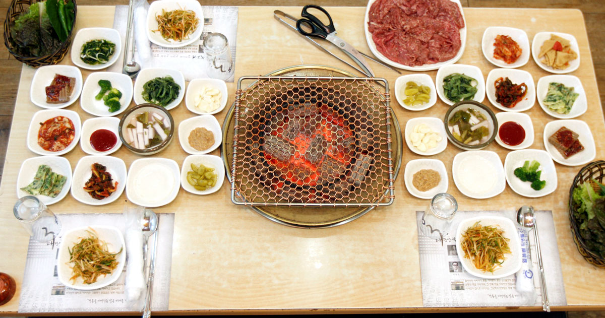 Thin marinated beef grilling over charcoal on a brass grill at Samdae Gwangyang Bulgogi